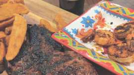 Steak on a cutting board after being grilled next to a plate of grilled shrimp.